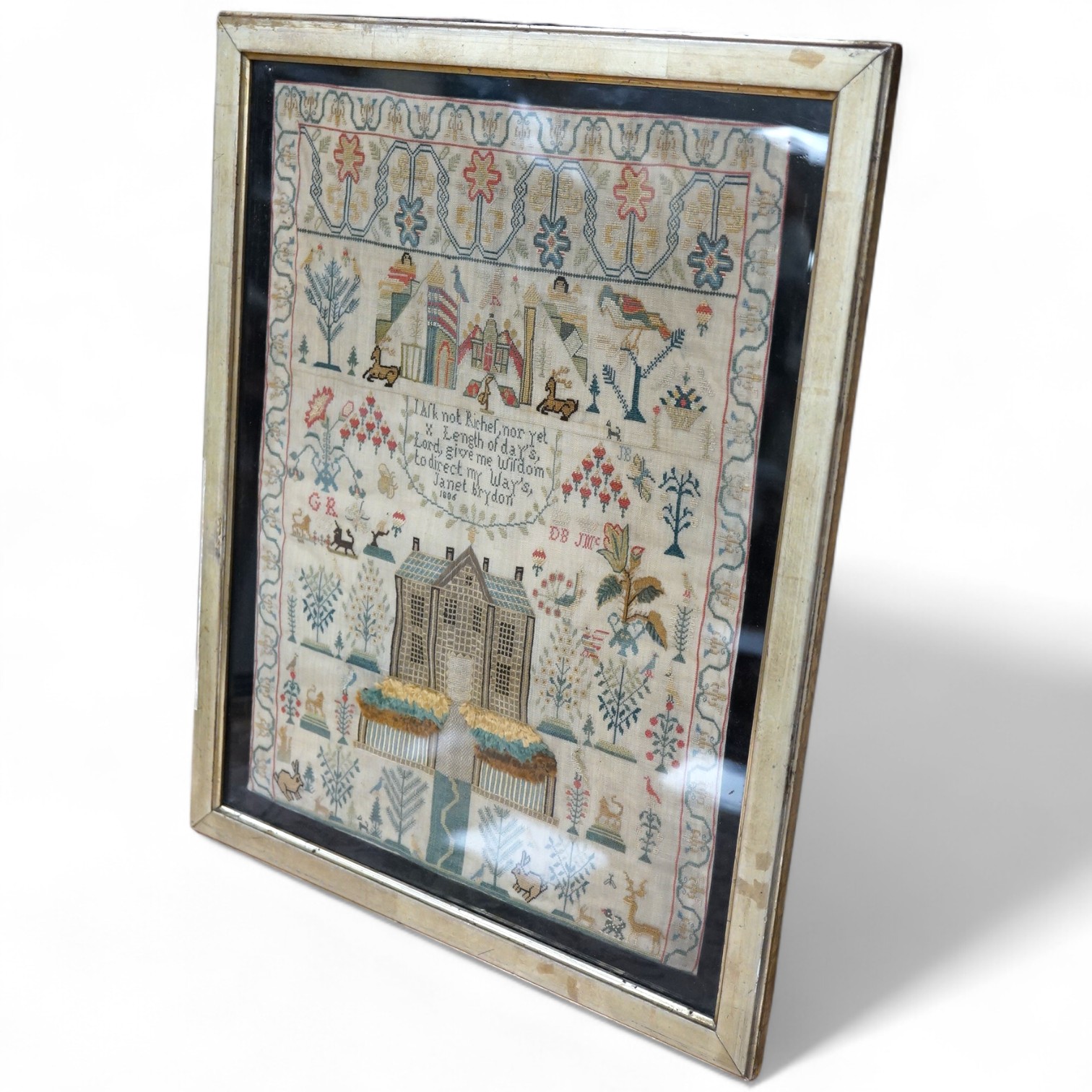A George lll needlework sampler dated 1806, by Janet Brydon. Worked on fine linen, the sampler embroidered with ornate motifs of angels, birds, deer, lions and a castle around a short embroidered script; I ask not riches